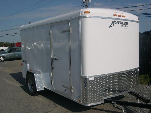a white Homesteader cargo trailer is parked in a gravel lot