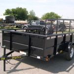a black trailer is parked in a parking lot next to a truck .