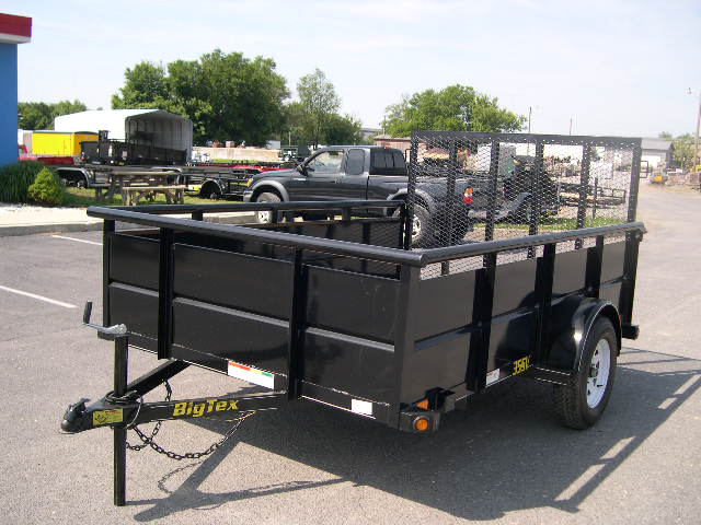 a black trailer is parked in a parking lot next to a truck .