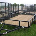 a trailer with a wooden deck is sitting on top of a lush green field .