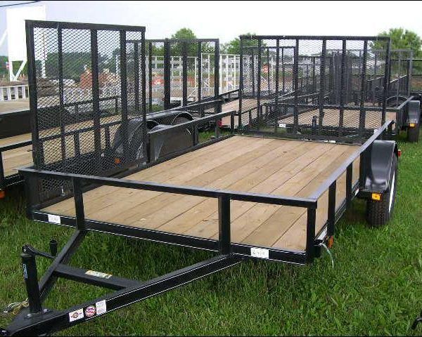 a trailer with a wooden deck is sitting on top of a lush green field .