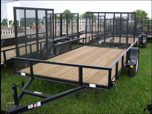 a trailer with a wooden deck is sitting on top of a lush green field .