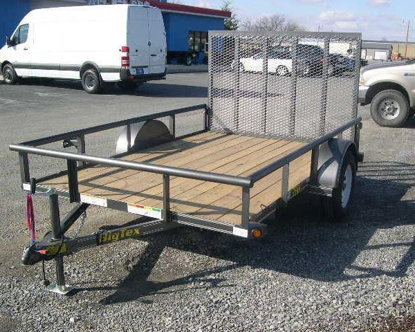 a small trailer is parked in a gravel lot next to a white van