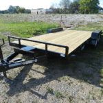 a trailer with a wooden deck is parked in a grassy field .
