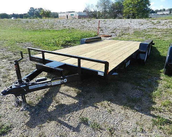 a trailer with a wooden deck is parked in a grassy field .