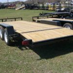 a black trailer with a wooden deck parked in a grassy field