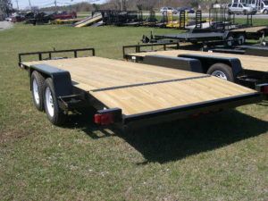 a black trailer with a wooden deck parked in a grassy field
