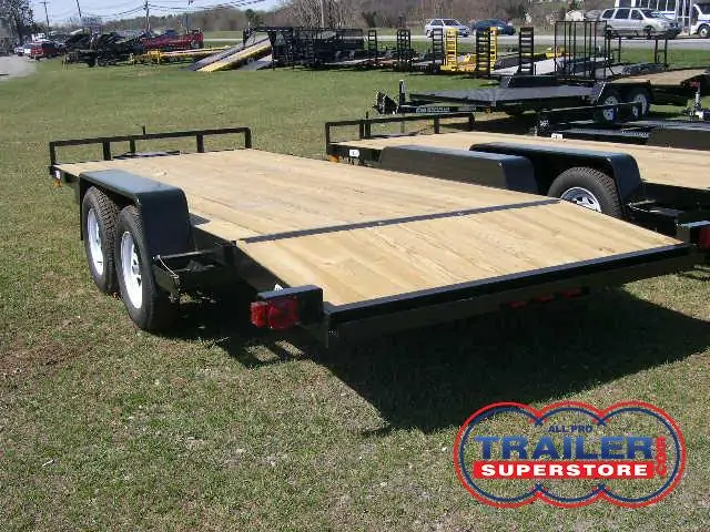 a black trailer with a wooden deck parked in a grassy field