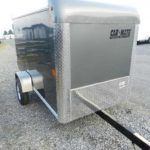 a gray trailer is parked in a gravel lot .