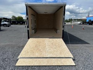 an atc trailer is sitting in a gravel lot with the door open .