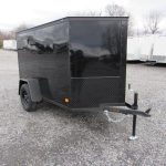 a black trailer is parked in a gravel lot .