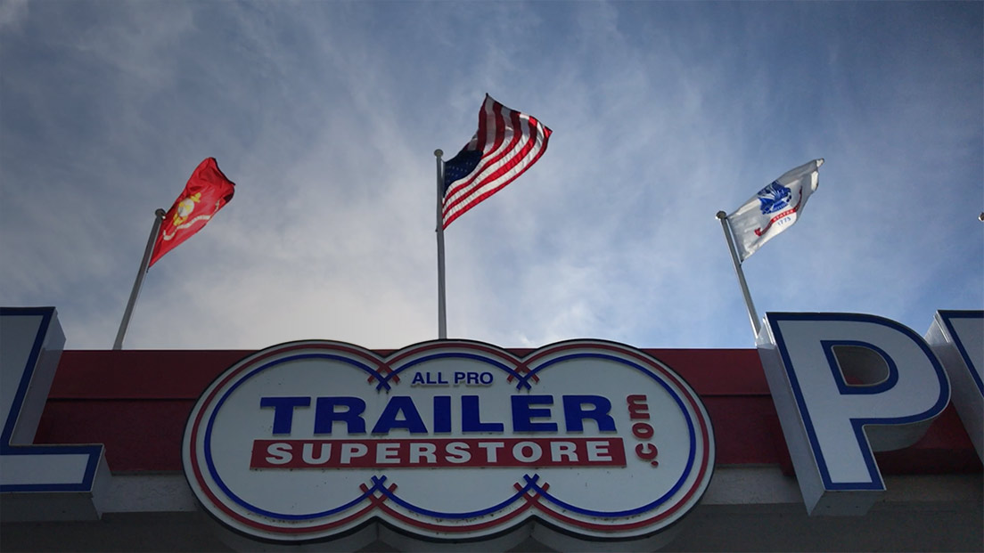 a trailer superstore sign with flags flying in the background
