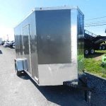 a black and silver trailer is parked on the side of the road in a parking lot .