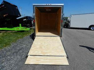 an empty trailer with a wooden ramp is parked on the side of the road .