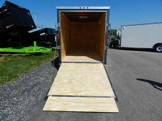 an empty trailer with a wooden ramp is parked on the side of the road .