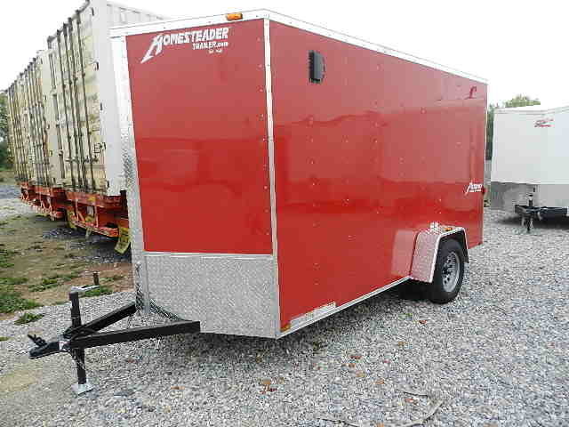 a red homesteader trailer is parked in a gravel lot .