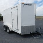 a white homesteader trailer is parked in a gravel lot