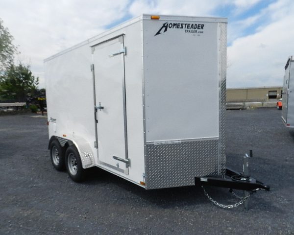 a white homesteader trailer is parked in a gravel lot