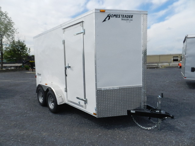a white homesteader trailer is parked in a gravel lot