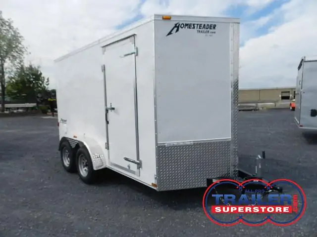 a white homesteader trailer is parked in a gravel lot