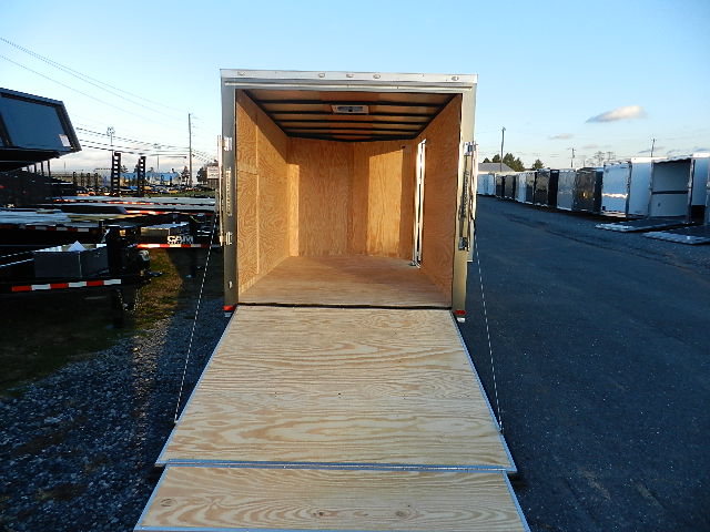 a covered wagon trailer with a wooden floor is parked on the side of the road .