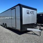 a gray and black trailer is parked in a gravel lot .