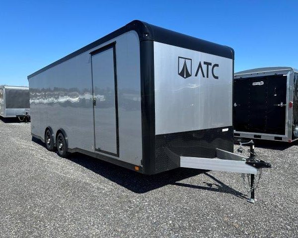 a gray and black trailer is parked in a gravel lot .