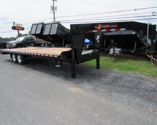 a flatbed trailer is parked on the side of the road next to a dump trailer .