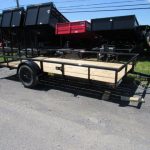a Big Tex trailer with a wooden deck parked next to a row of dump trailers