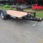 a small trailer with a wooden deck is parked on a gravel road