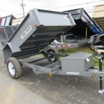 a gray dump trailer is parked on the side of the road .
