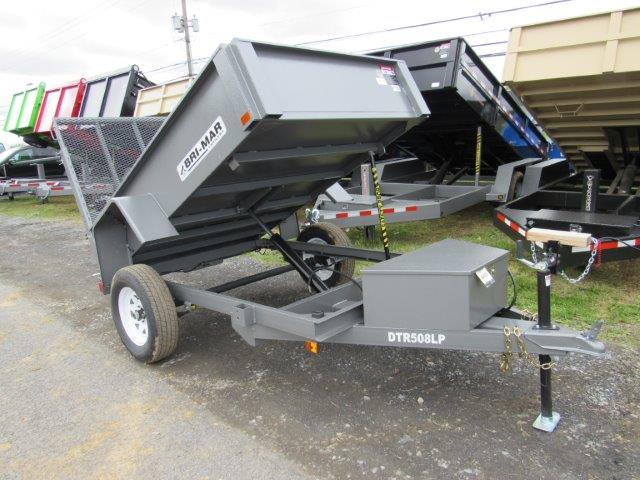 a gray dump trailer is parked on the side of the road .
