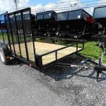 a black carry-on ATV trailer with a wooden deck is parked on a gravel road