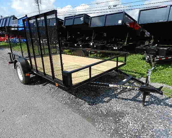 a black carry-on ATV trailer with a wooden deck is parked on a gravel road