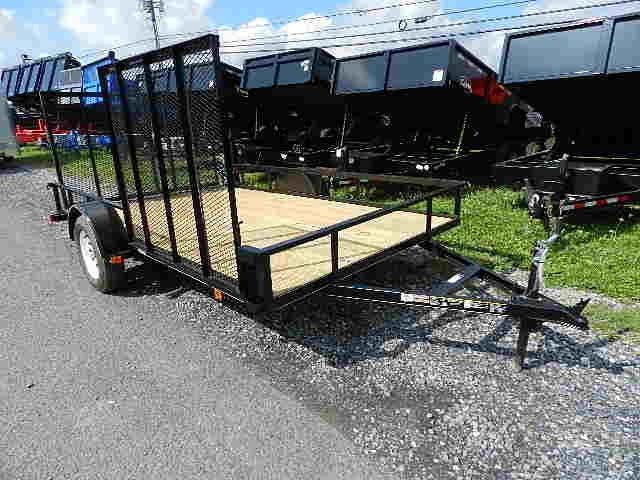 a black carry-on ATV trailer with a wooden deck is parked on a gravel road