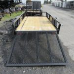 a trailer with a wooden deck and a metal ramp is parked on the side of the road .
