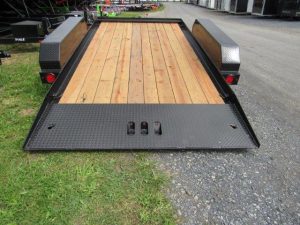 a trailer with a wooden deck is parked on a gravel road .