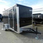 a black trailer is parked on the side of the road next to a dumpster .