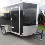 a black trailer is parked on the side of the road next to a dumpster .