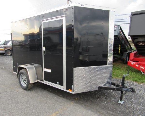a black trailer is parked on the side of the road next to a dumpster .