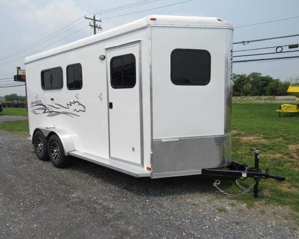 a white horse trailer is parked in a gravel lot .