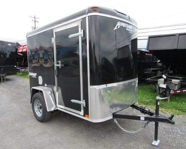 a black trailer is parked on the side of the gravel parking lot