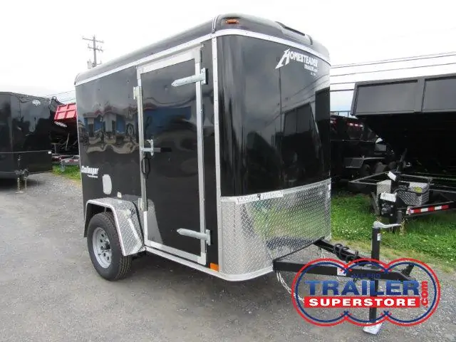 a black trailer is parked on the side of the gravel parking lot