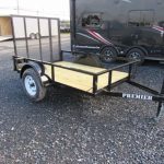 a small trailer is parked in a gravel lot next to a black trailer .