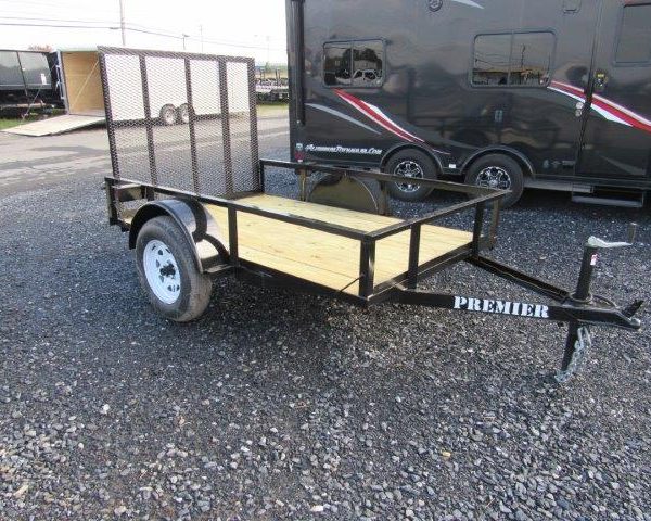 a small trailer is parked in a gravel lot next to a black trailer .
