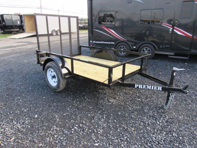 a small trailer is parked in a gravel lot next to a black trailer .