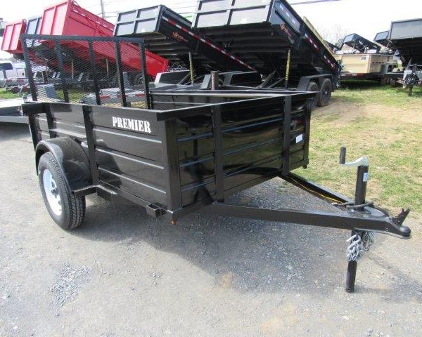 a black trailer is parked in a grassy field next to a dump truck .