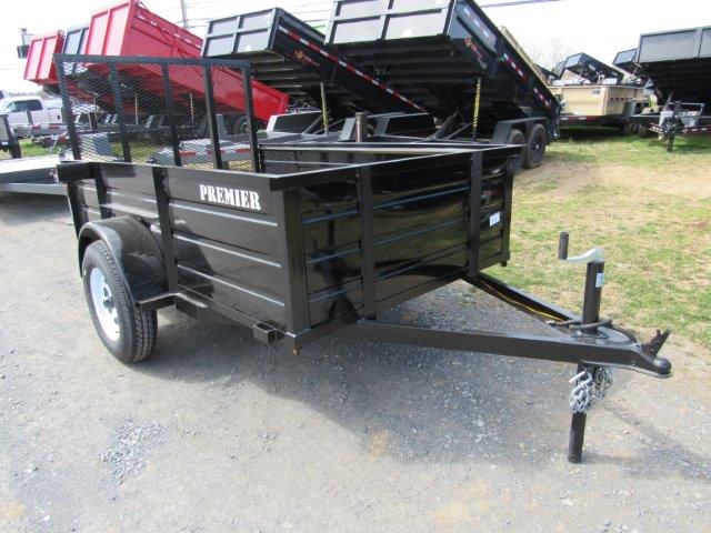 a black trailer is parked in a grassy field next to a dump truck .