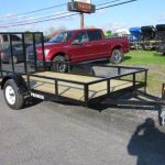 a black trailer with a wooden deck is parked on the side of the road