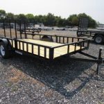 a trailer with a wooden deck is parked in a gravel lot .
